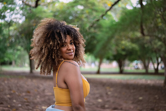 mulher negra de cabelos cacheados sorrindo em um parque com folhas secas no ch√£o