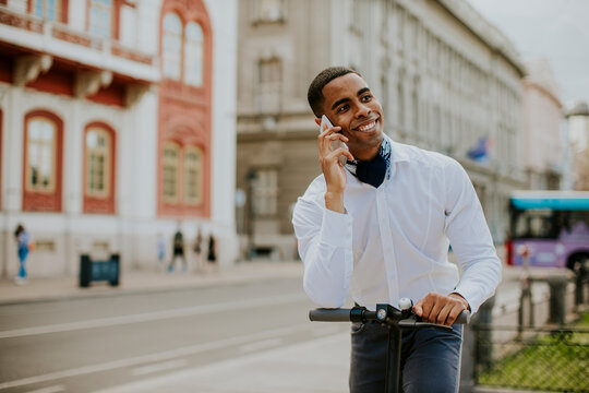 Young African American using mobile phone while standing with electric scooter on a street