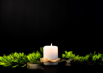 Scena con una candela bianca accesa legata con un fiocco dorato e circondata da rami di abete verdi. Con spazio per scrivere. Condoglianze. Anniversario. Commemorazione. Lutto. © Lavinia
