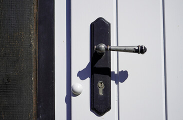 Old black metal door handle on a white wooden door. Close-up of locked door with keyhole.