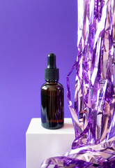 Brown serum jar mockup with pipette and holiday tinsel on cube podium on violet background,...