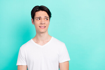 Photo of distrust brunet hairdo young guy look empty space wear white t-shirt isolated on vivid teal color background