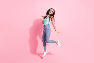 Full length body size photo of smiling woman wearing sunglass jumping up happy isolated on pastel pink color background