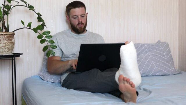 Full body of bearded man typing on laptop doing research. Male professional using computer sitting at home on bed with broken leg.
Busy freelancer working on modern tech notebook device. Money tree