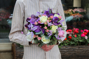 A guy holding a small bridal bouquet of flowers. White roses purple vanda orchid pink spray roses.