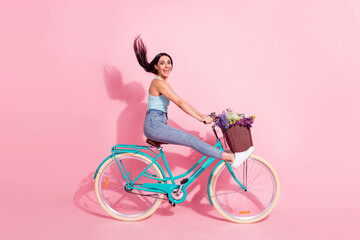 Full length body size photo of smiling woman riding bicycle isolated on pastel pink color background