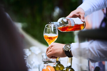 The waiter serves rose and white wine from the wine bottle in the wine glass at an event.