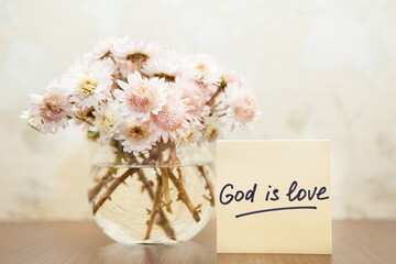 God is love - christian lettering, biblical phrase and bouquet of pink flowers in vase