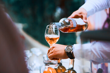 The waiter serves rose and white wine from the wine bottle in the wine glass at an event.