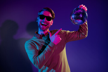 Photo portrait of man smiling in sunglass pointing finger disco ball music isolated purple color background