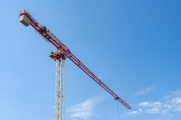red and white construction crane on a blue sky background. The building of the new houses and construction of buildings in the city.