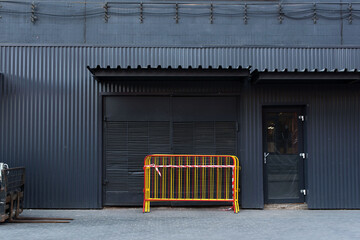 Corrugated gray metal facade. Metal movable fence in a bundle. Fan barrier. temporary fence against the backdrop of a metallic grey facade. Black glass door