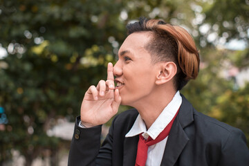A young male student makes a mocking shh gesture barely containing his laughter. Delinquent doing...