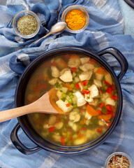 Jewish national cuisine. Vertical food composition with large pot with hot Jewish chicken soup and spices on a blue background. Healthy and tasty food. Flat lay