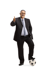 Full length portrait of a mature man in suit and tie stepping on a soccer ball and gesturing thumbs up