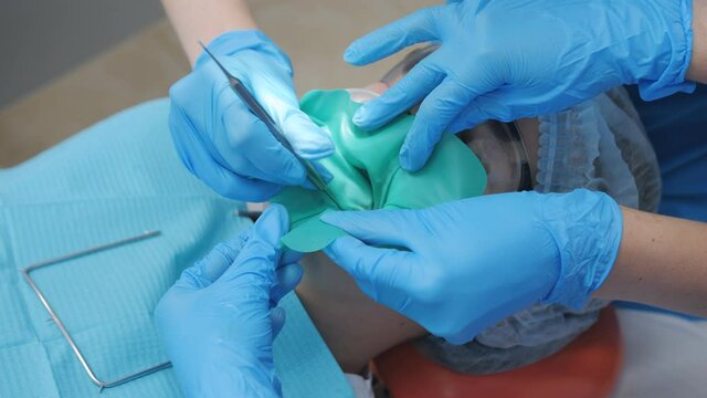 A dentist and an assistant install a cofferdam in the oral cavity of a teenage girl patient.