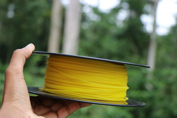 Printer filament made from Bio plastic held in hand with nature on background to show concept of...