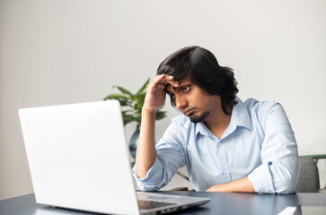 Exhausted and upset indian businessman looks at the laptop screen with disappointment, overworked and burnout concept