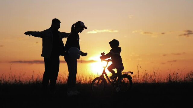 Happy family. Silhouette of a young family with a little son. Kid is learning to ride a bike. Silhouettes family with the child stand in a sunset. Teamwork, holding hands. Happy family concept.