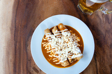 Drowned Mexican flutes, traditional Mexican food with red sauce. Drowned tacos. Traditional Mexican food. Mexican food on wooden background. Traditional Mexican food concept.