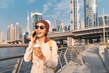 Asian Woman in a headscarf drinking coffee and talks and gossips on the phone with a friend on the...