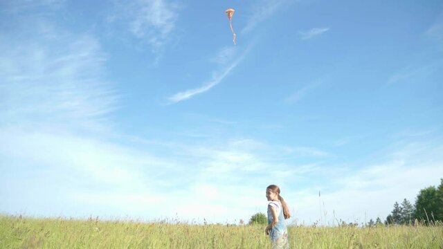 Girl launching and controlling 
a flying a colorful kite on the blue sky background Happy childhood moments or outdoor time spending concept image. 