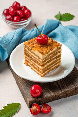 A piece of honey cake decorated with fresh cherries on a light background.
