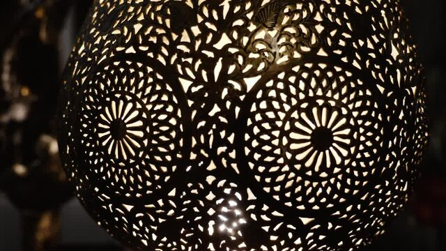 A lit, Moroccan, Arabic brass lamp with intricate floral pattern. Concept for Moroccan and Arabian lamp design. Zooming in through the pattern into the inside of the lamp.