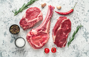 Assorted raw beef steaks. Tomahawk steak and ribeye steaks on light stone background