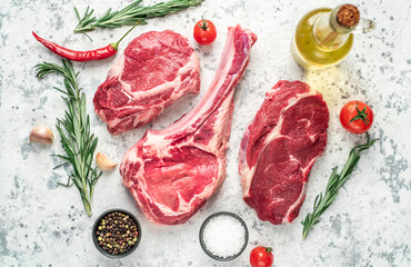 Assorted raw beef steaks. Tomahawk steak and ribeye steaks on light stone background