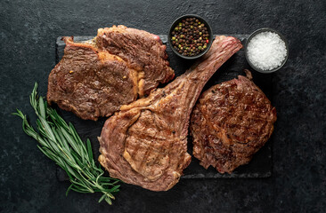Variety of grilled beef steaks. Grilled tomahawk steak and ribeye steaks on stone background