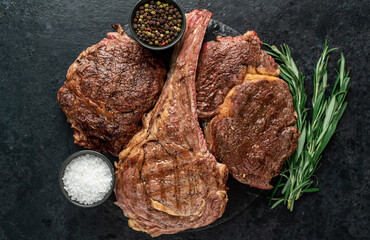 Variety of grilled beef steaks. Grilled tomahawk steak and ribeye steaks on stone background