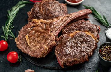 Variety of grilled beef steaks. Grilled tomahawk steak and ribeye steaks on stone background