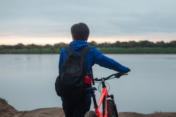 Young man with headphones walking with his bike beside him, appreciating the scenery, active lifestyle.