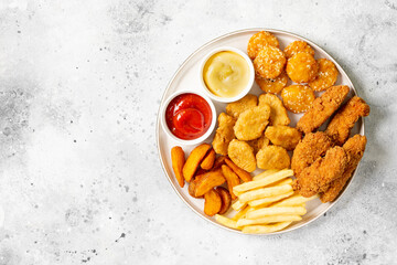 Chicken nuggets, strips, french fries, fried potatoes, ketchup and cheese sauce on a light background. Fast food top view	