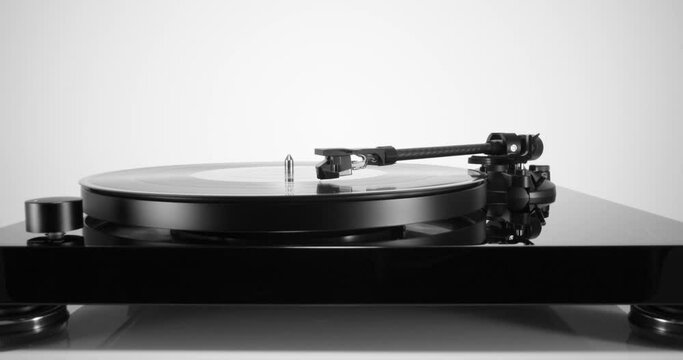 Front view of black turntable with spinning vinyl record on white. Push in to the tonearm headshell