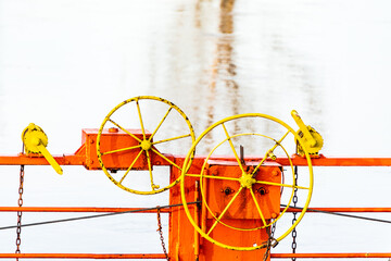 The details of the cable ferry which across a river by cables connected to both shore. The orange chain ferry, yellow steering wheel and blue water