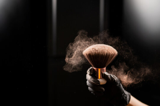 A Woman Shakes A Large Powder Brush With Clouds Of Dust On A Black Background. Treatment After Instant Tanning