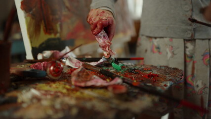 Unknown people spending time in workshop. Painter hand mixing paint on palette.
