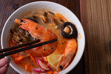 miso soup with mussels, shrimps , shiitake mushrooms and vegatables. served at dark brown wooden table. flat lay