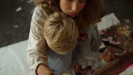 Creative female painter creating artwork with children on easel in art studio.