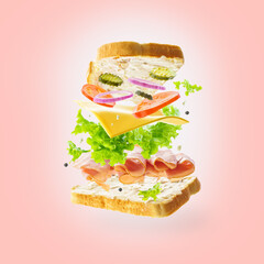In the photo we see a sandwich with different ingredients in a state of levitation. Pale pink background. There are no people in the photo. High angle view. Careful viewing.
