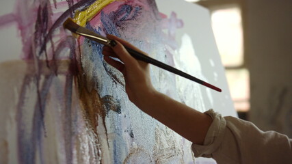 Young woman drawing at workplace. Creative painter making brush stroke indoors.