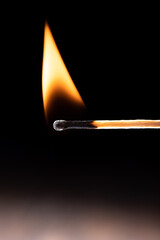 Triangular flame on a burning match against a black background.