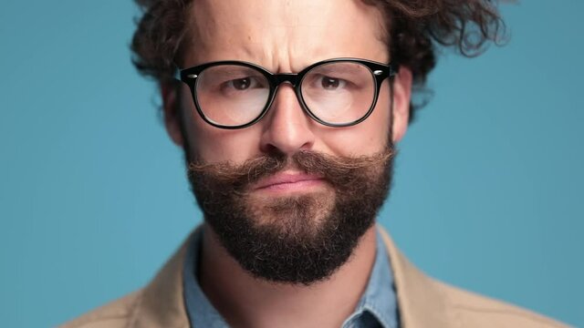 thoughtful casual man with long beard and moustache making a suspicious face, holding hand to chin, thinking and nodding on blue background in studio
