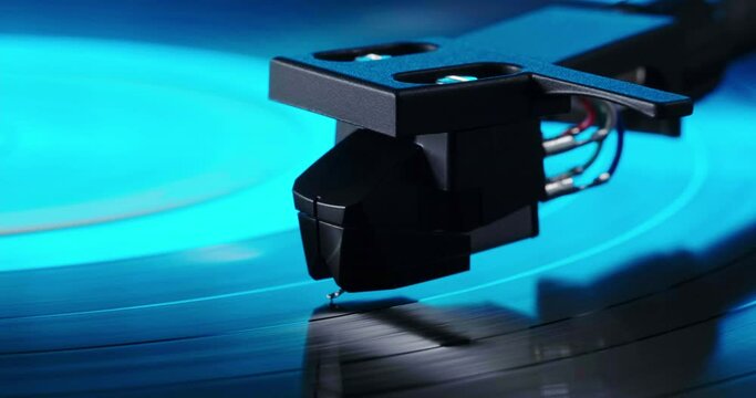 Extreme closeup of tonearm headshell on spinning vinyl record. Party neon blue light on turntable