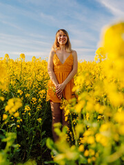 Naklejka na ściany i meble Attractive cheerful woman on rapeseed field with sunset. Yellow flowers and happy woman