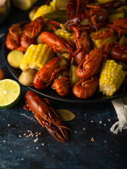 Against a dark blue background, we see a beautiful still life of boiled pieces of yellow corn and red crayfish. Also, half a lemon and a large crayfish lie near the plate. Macro photography. Close-up.