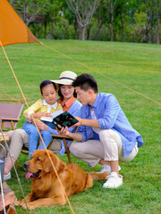 Happy family of three and pet dog reading outside