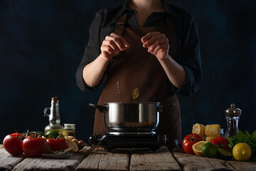 In the photo we see the process of cooking seafood with vegetables. The cook adds spices to the pot. On a wooden table, we see a beautiful still life made from different ingredients. Blue background.